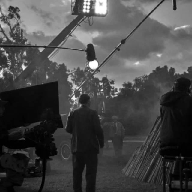 Behind-the-scenes view of a film crew working on an outdoor production set with cameras, lighting equipment, and technicians.